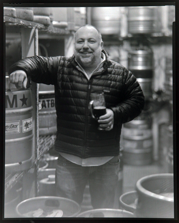 Jimmy Carbone at brewery with beer tanks and glass, circa 2011 for Brewer's Choice event preview